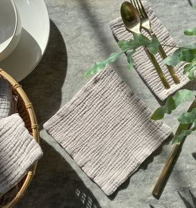 Small light gray gauze napkin on a marble tabletop with gold silverware. Napkin made by Charley Charles. 