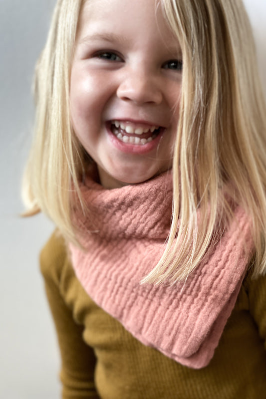 Young girl wearing a thick Charley Charles Bandana Style Bib in the color Dusty Blush Pink. 